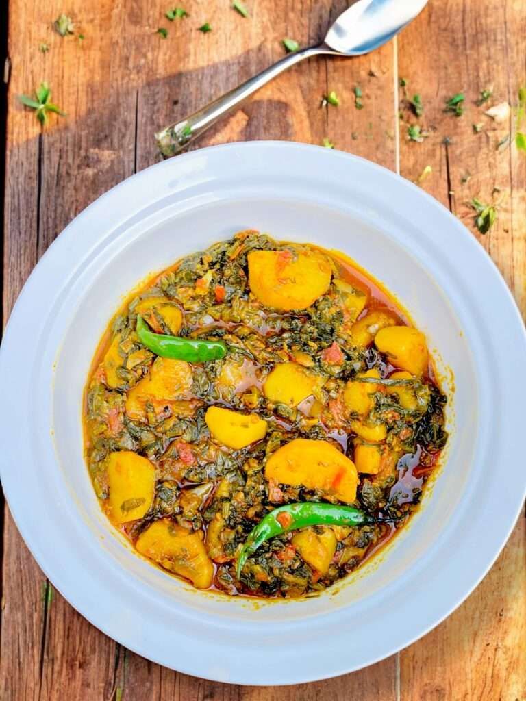 aloo palak arranged in white bowl placed on wooden countertop.