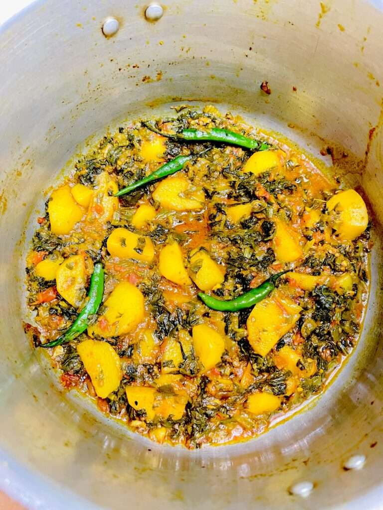aloo palak arranged in silver pan garnished with green chilies.
