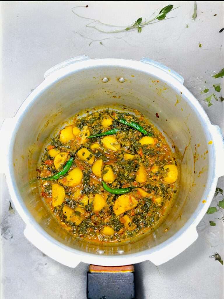 aloo palak arranged in silver pan placed on concrete countertop garnished with green chilies.