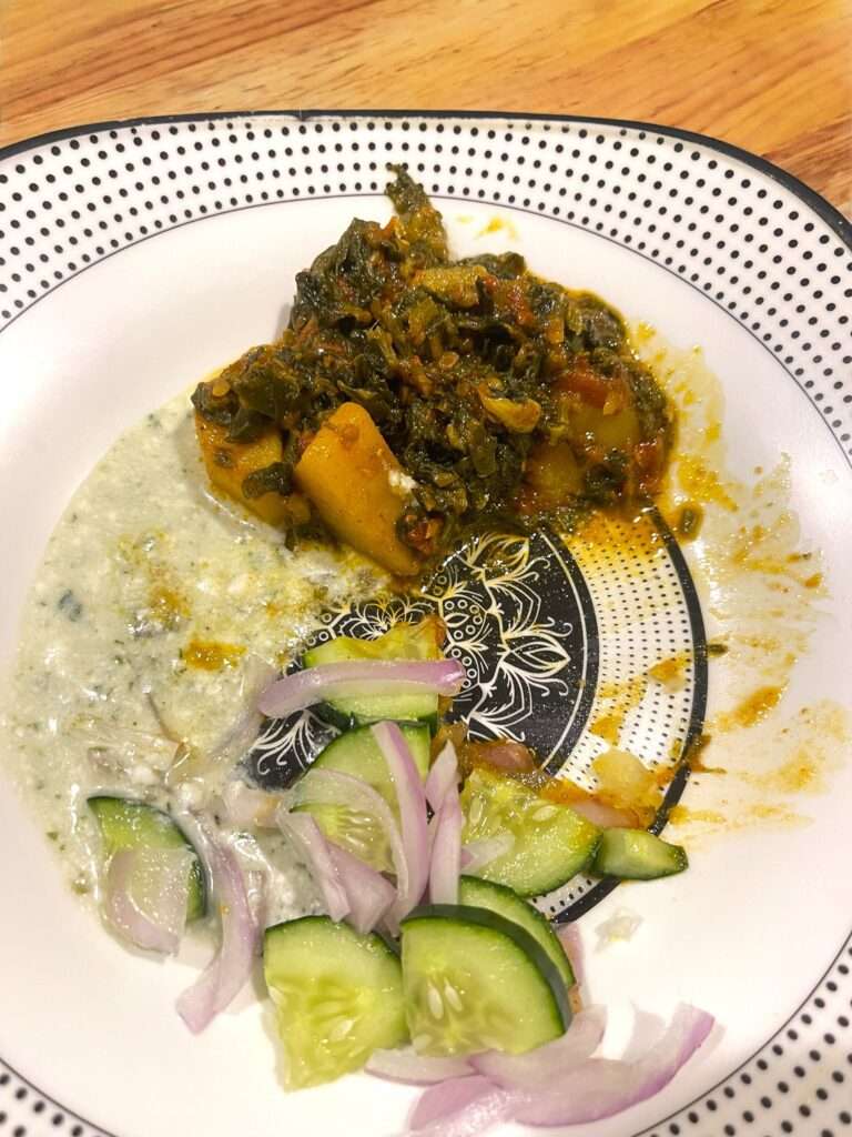 aloo palak arranged in white plate along with side of raita and salad.