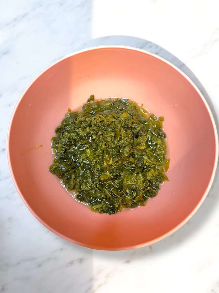 boiled spinach arranged in pink bowl placed on marble countertop.