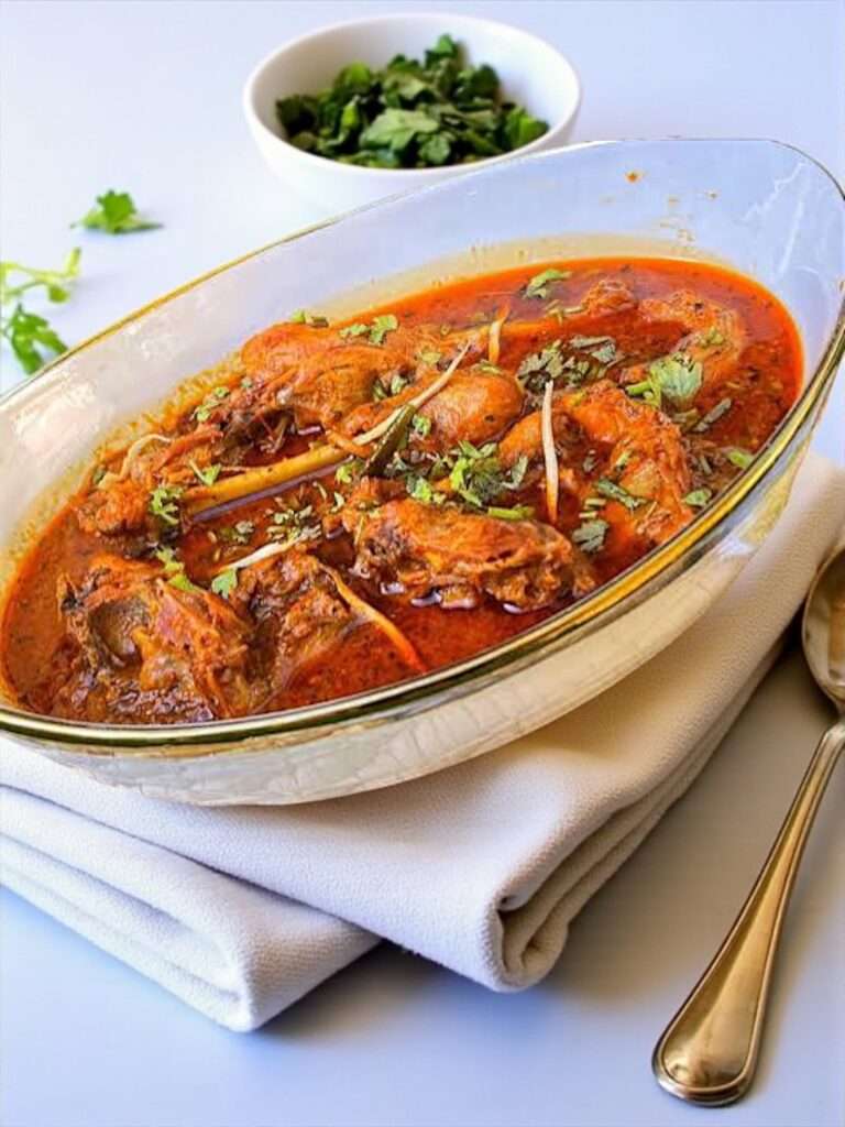 Desi Chicken Curry served in white dish garnished with cilantro, placed on white kitchen towel on marble surface.