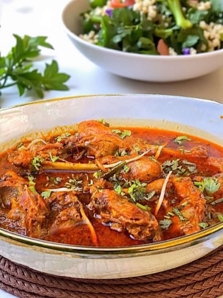 Desi Chicken Curry served in white dish garnished with cilantro, placed on white kitchen towel on marble surface.