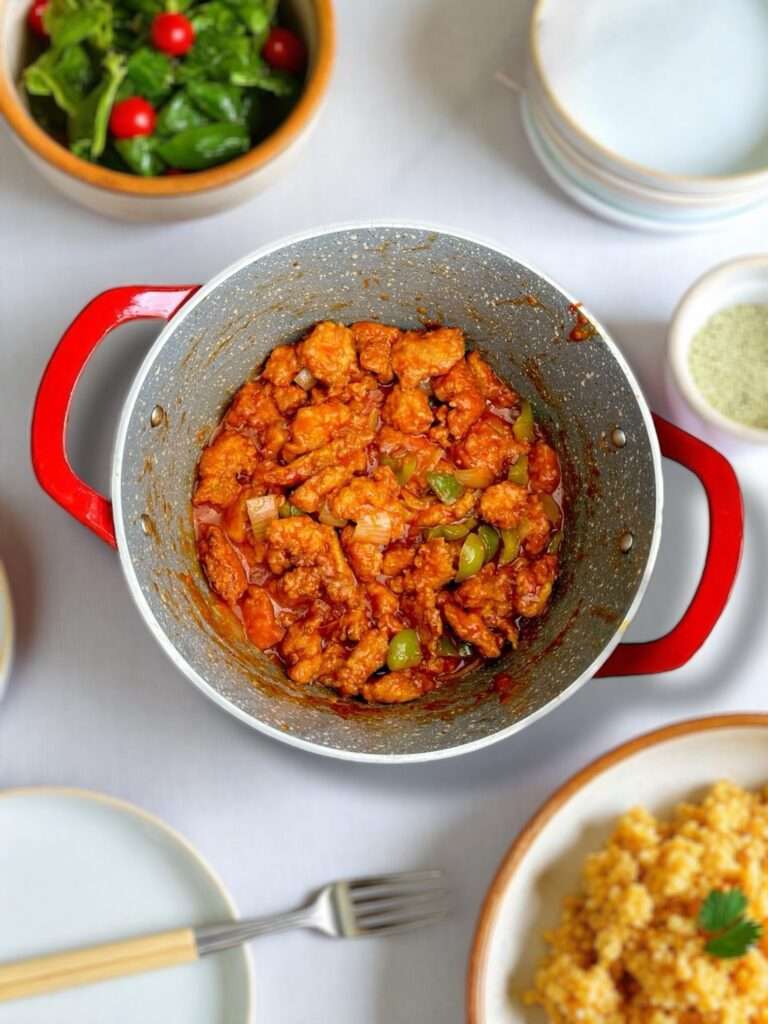 Chicken Manchurian arranged in red handled marble pot, placed on white marble countertop.