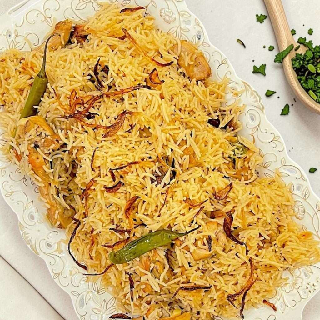chicken pulao arranged in white rice dish, placed on grey kitchen surface.