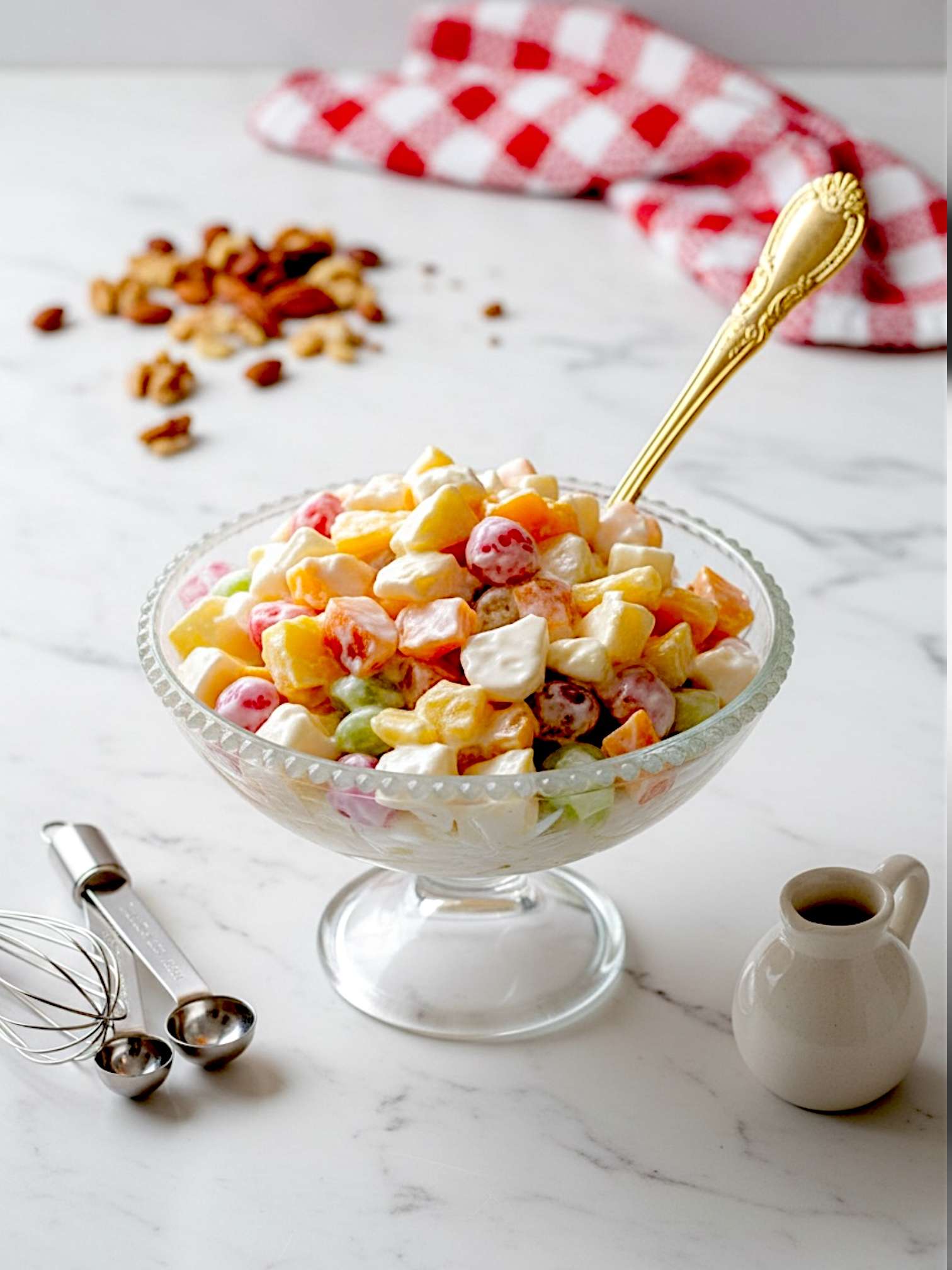 Cream fruit chaat arranged in dessert bowl, placed on messy marble surface, milk pot and a hint of red white check kitchen cloth placed in the background.