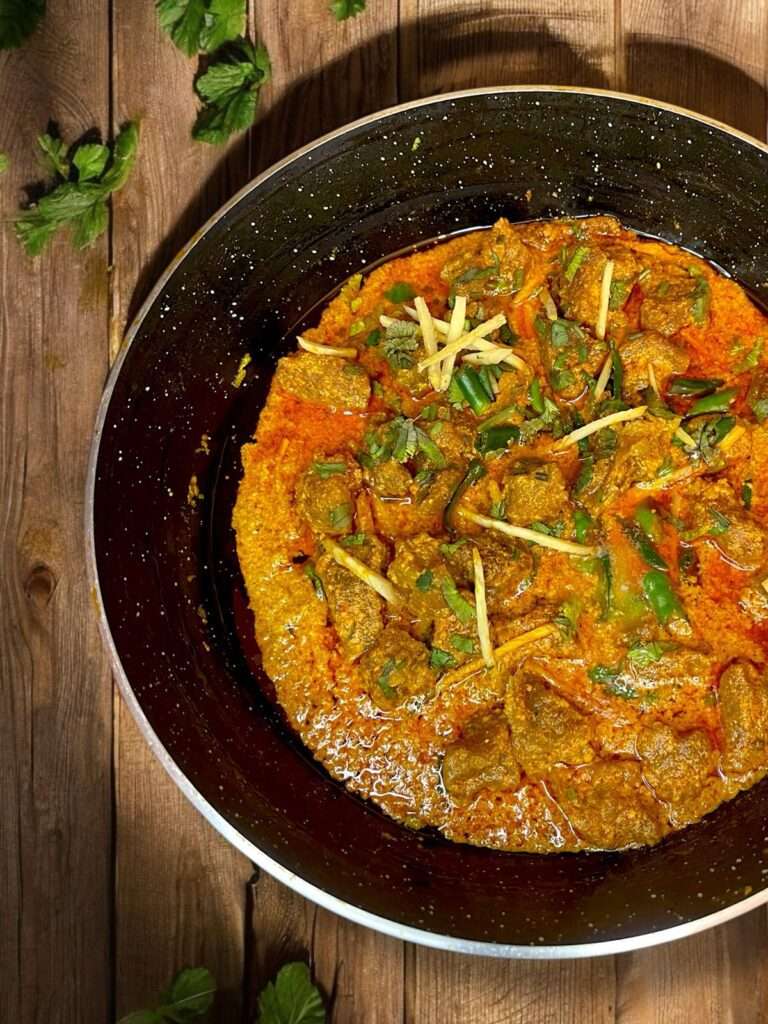 beef tikka masala in black wok arranged on wooden table.