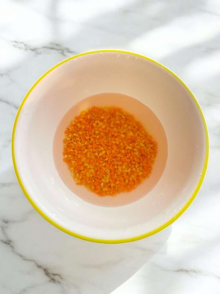 Moong masoor dal soaked in bowl arranged in white bowl placed on marble countertop.