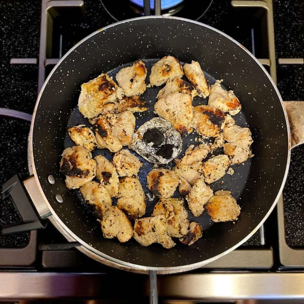 Chicken Malai Tikka arranged in a black pan on the stovetop, ready to be infused with coal smoke.