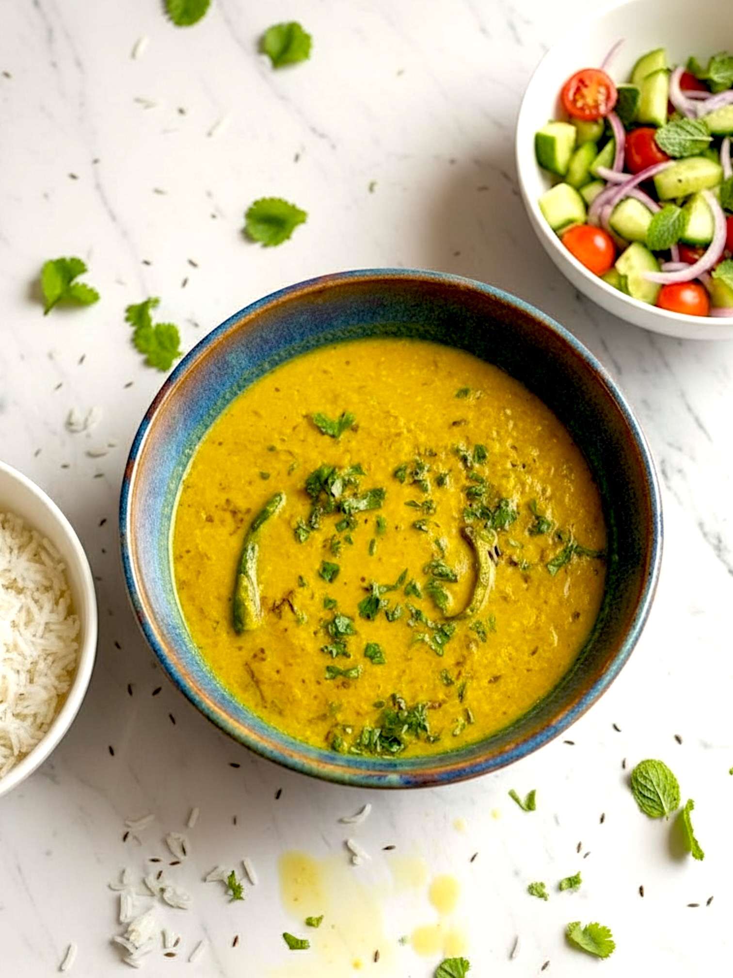 Moong masoor dal arranged in vibrant ceramic bowl, along with a side of white rice bowl, some fresh salad, placed on messy marble surface.