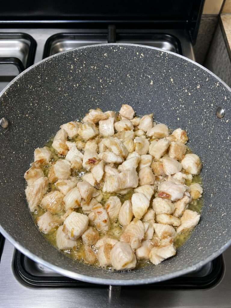 Boneless chicken pieces cooking with sautéed onions in a pan