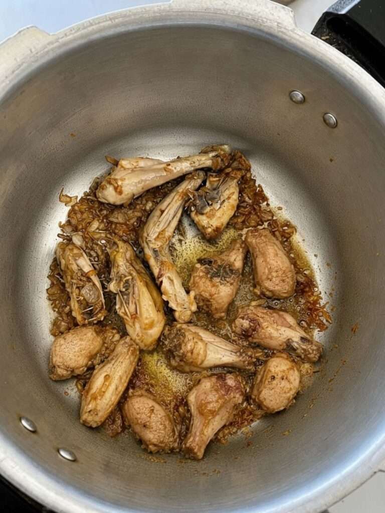 Chicken pieces cooking with golden fried onions in a large pot