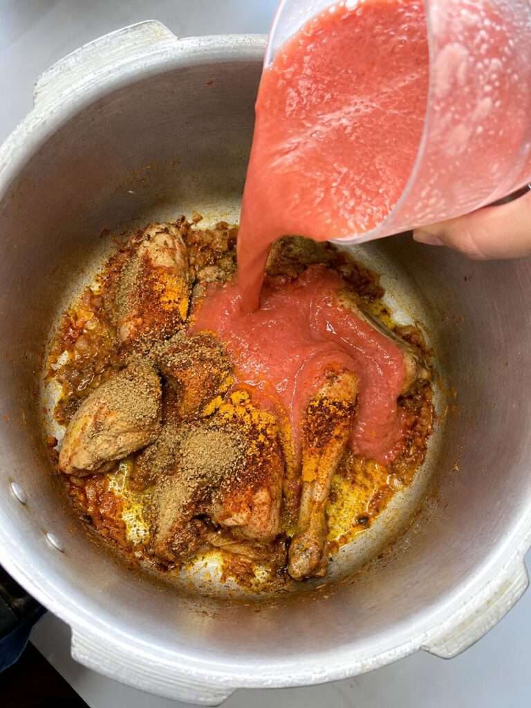 Chicken with spices and blended tomatoes being added to the cooking pot