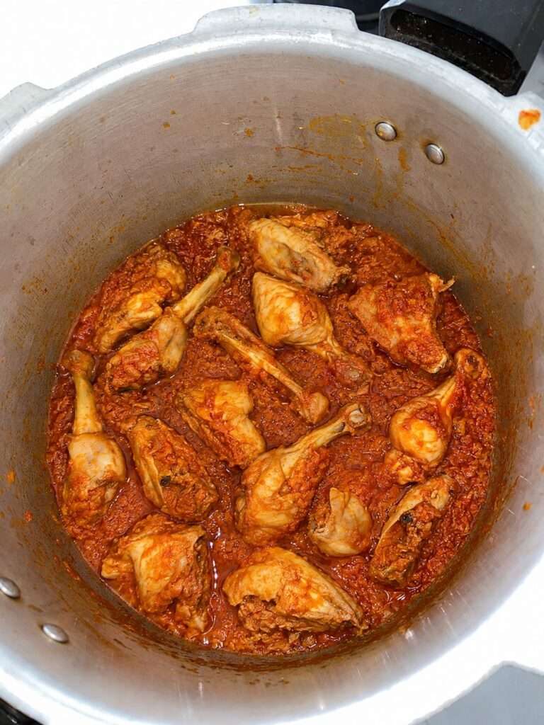 Chicken pieces simmering in rich red curry gravy