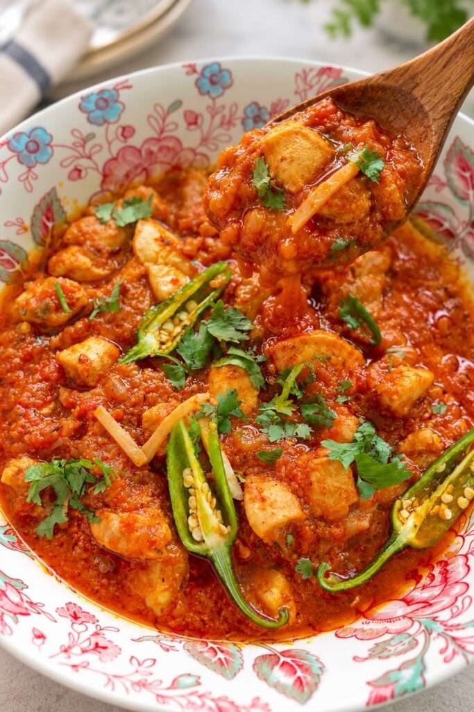 Spoonful of chicken ginger curry with tender chicken, tomato gravy, ginger, and cilantro