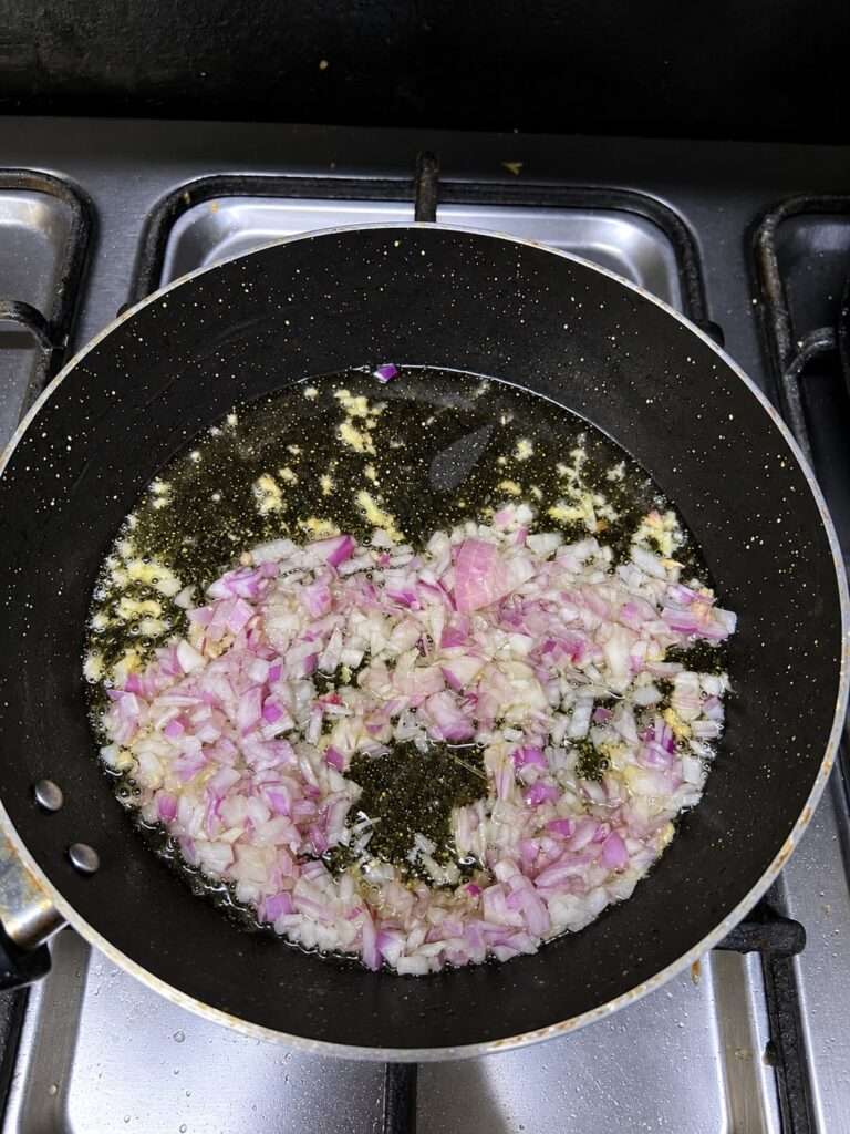 Finely chopped onions sautéing in oil in a same black pan