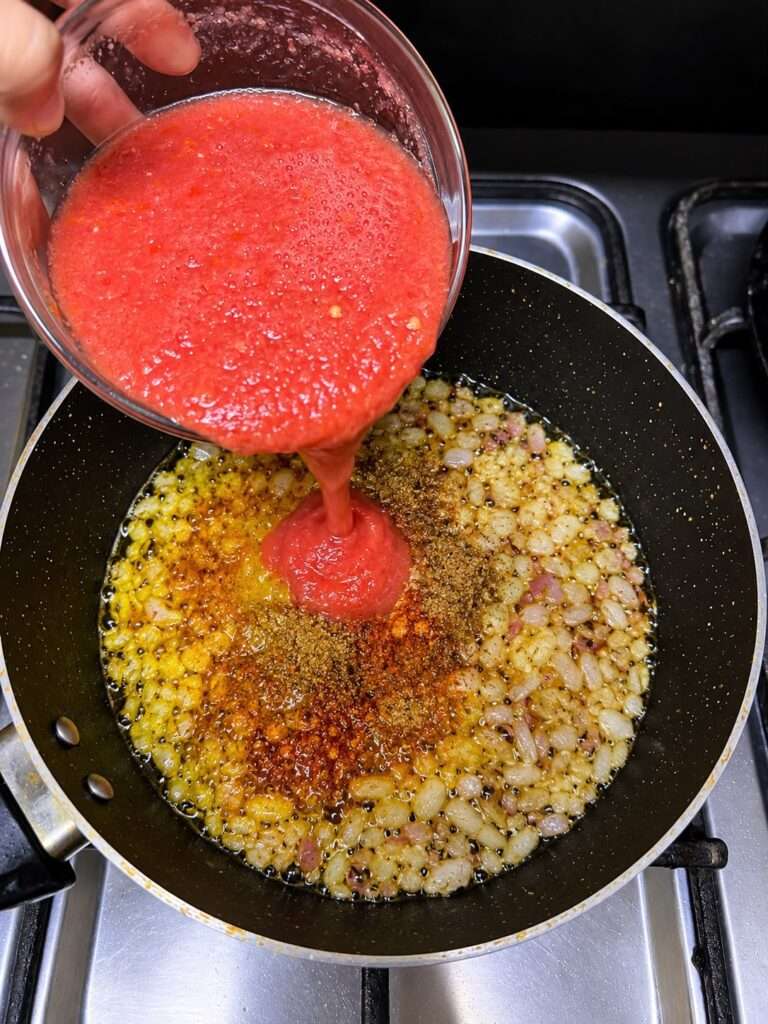 Tomato puree and spices being added to sautéed onions in a pan
