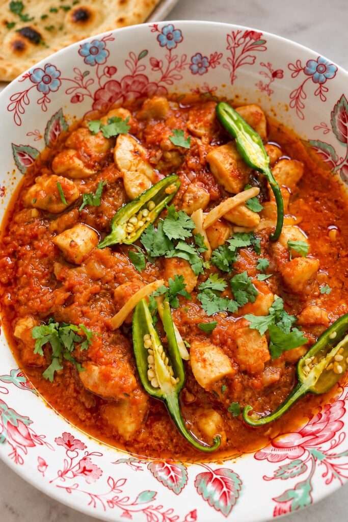 Close-up of spicy chicken ginger curry garnished with green chilies, cilantro, and ginger