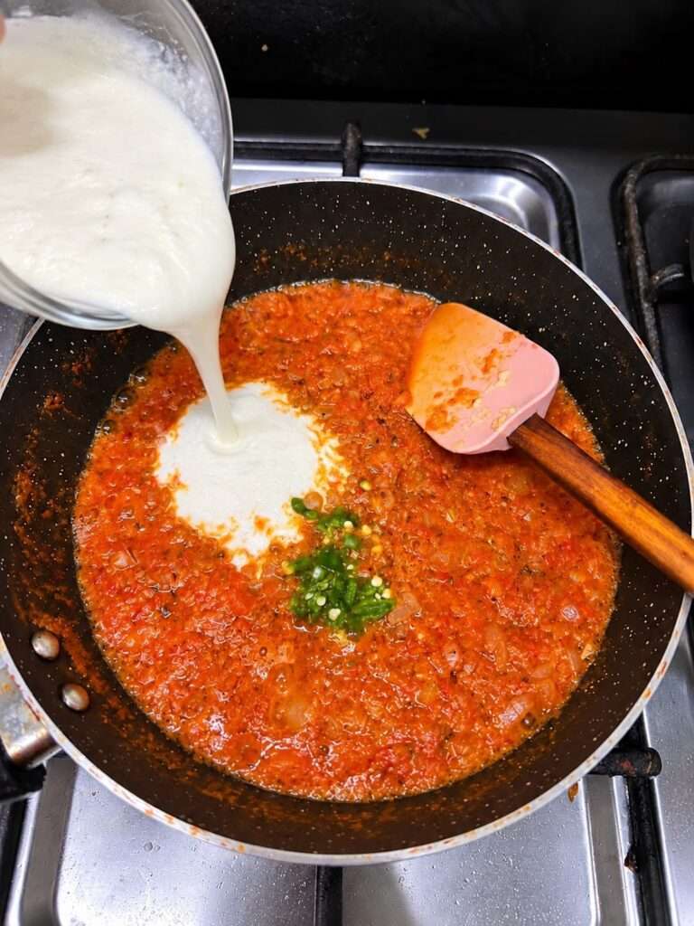 Yogurt and green chili paste being added to tomato onion masala with green chilies for chicken ginger curry