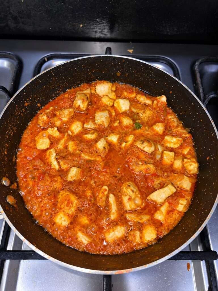 Fried chicken pieces added to a rich tomato masala in a pan