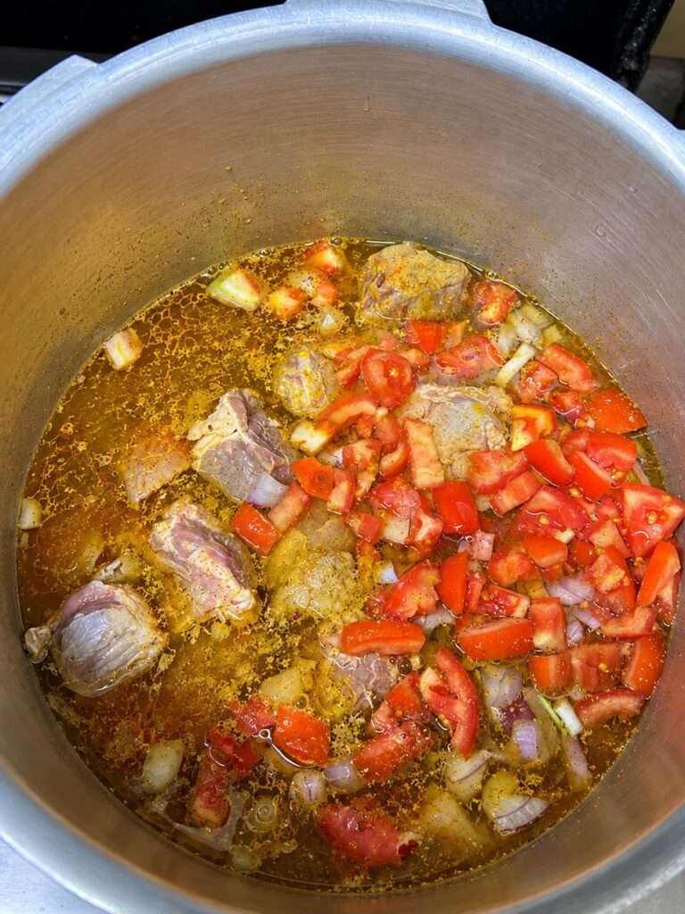 Meat cooking with ginger garlic paste, onions, tomatoes, and spices